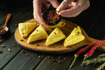 The chef hands add aromatic seasoning to the thin rolled pancakes. Concept of cooking dinner on the...