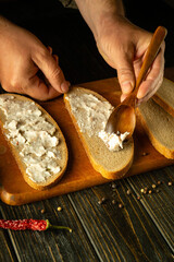 Preparing sandwiches on the kitchen table for a snack. A spoon in the hands of a chef for spreading lard on sliced rye bread. Place for advertising