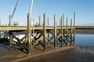 Fototapeta na wymiar Serene boat dock with sailboats at low tide, clear blue skies, calm waters, in a picturesque rural landscape