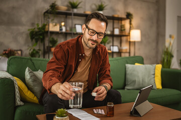 Adult caucasian man sit on sofa and drink medical pills at home