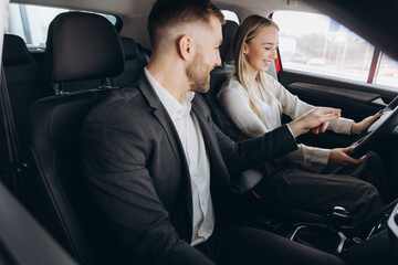 Competent car dealer showing female customer interior of luxury auto. Caucasian man and woman sitting inside and talking. Concept of selling and purchase.