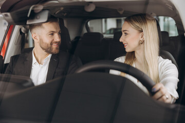 Competent car dealer showing female customer interior of luxury auto. Caucasian man and woman...