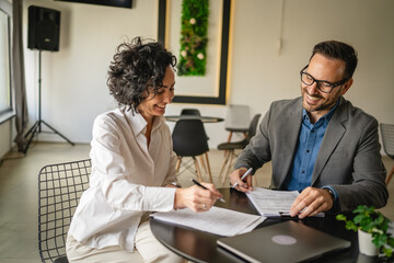Mature woman sign insurance or contract to adult man in cafe