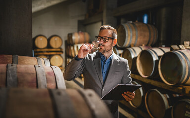 Adult man winemaker hold glass stand between the barrels in cellar