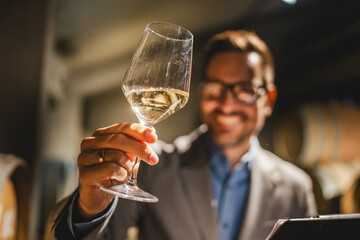 Adult man winemaker hold glass of white wine in winery