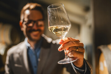 Adult man winemaker hold glass of white wine in winery