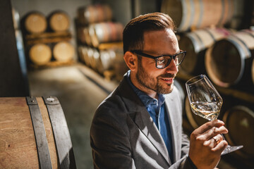 Adult man winemaker hold glass stand between the barrels in cellar