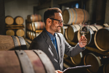 Adult man winemaker hold glass stand between the barrels in cellar