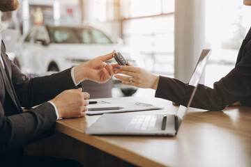 Close-up of a manager handing the car keys to a new owner to a woman at a table with a laptop in a...