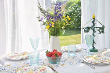 Table setting for the Midsommar holiday. On the table there is a vase with wildflowers, strawberries, a pole.Glad midsommar