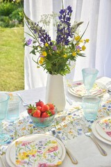 Table setting for the Midsommar holiday. On the table there is a vase with wildflowers, strawberries.Glad midsommar