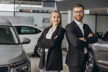 Smiling, friendly car sellers standing in car salon with arms crossed and announcing retail.