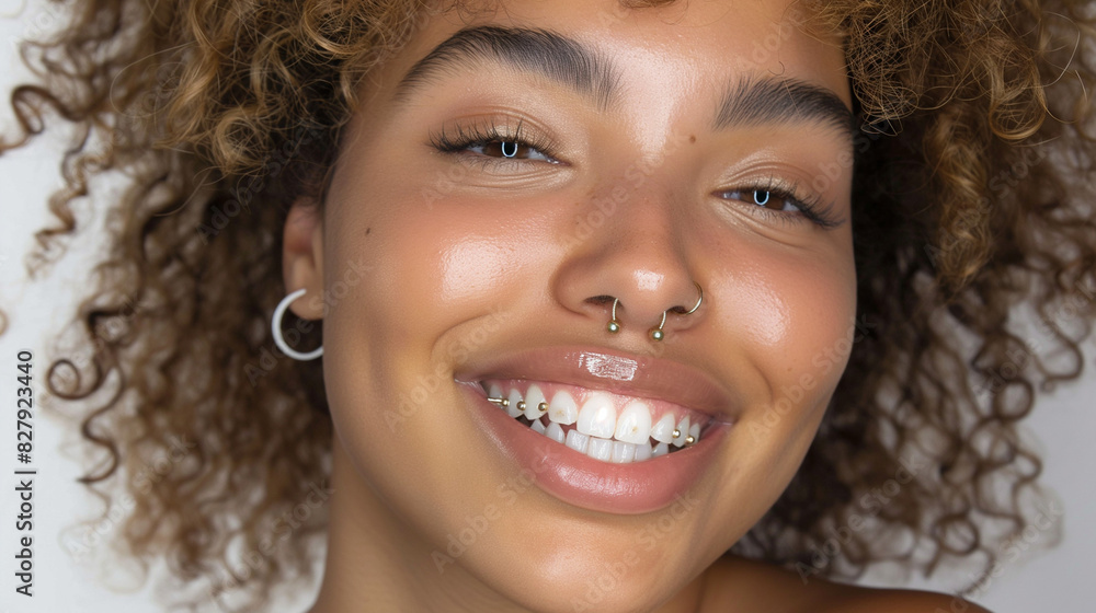 Wall mural Portrait of a beautiful smiling woman with afro hair, nose ring, and ear piercings, wearing earrings. The photo features a white background, professional photography, professional color grading, soft 