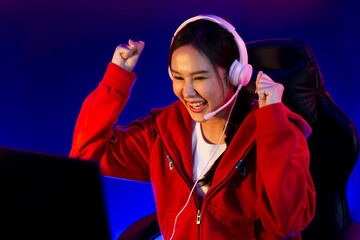 Host channel of smiling beautiful Asian girl streamer playing with raising fist up winning on Esport skilled team players wearing headphones pastel color, fighting online game at neon room. Stratagem.