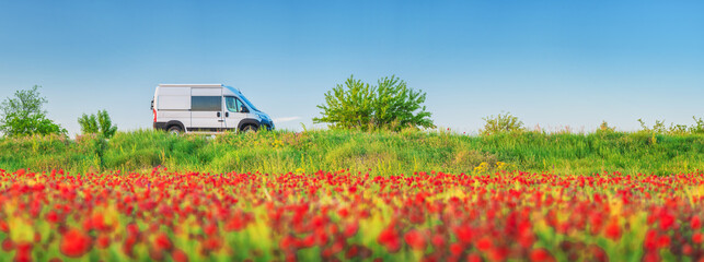 panorama landscape with field of red poppies and white van on road under blue sky with copy space