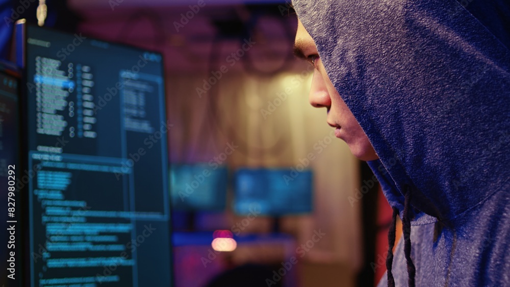 Poster extreme close up on hacker in graffiti painted hideout focused on developing spyware software, using