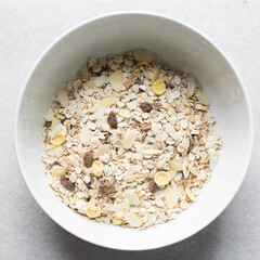 Top view of oat muesli in a white ceramic bowl, overhead view of muesli with oats almonds raisins and cornflakes in a white breakfast bowl, prepping healthy granola breakfast bowl