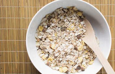 Top view of oat muesli in a white ceramic bowl, overhead view of muesli with oats almonds raisins and cornflakes in a white breakfast bowl, prepping healthy granola breakfast bowl