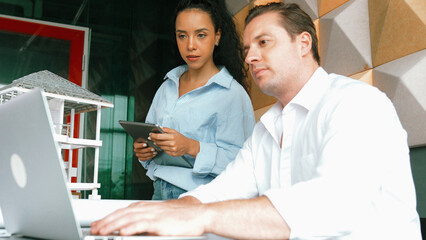 Portrait of project manager pointing at house model while discussion about building design. Caucasian cooperative architect engineer team brainstorming about building material. Teamwork. Manipulator.