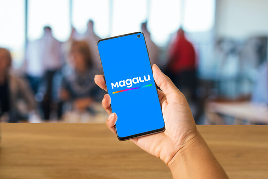 hand holding cell phone with the Magalu logo and blurred people in the background, Rio de Janeiro, Brazil, May 2024