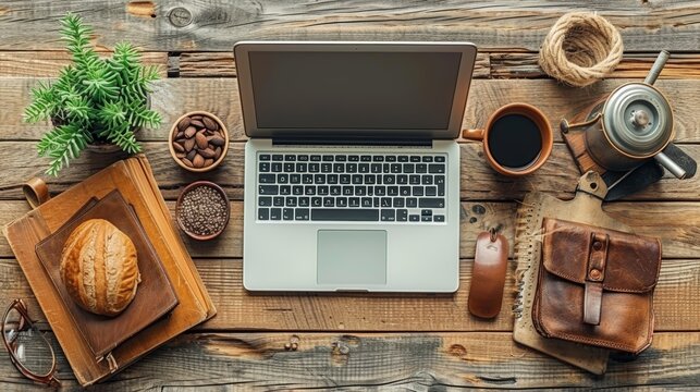 A beautifully arranged wooden desk featuring an open laptop, various office supplies, a cup of black coffee, a potted plant, and a loaf of bread on a wooden board
