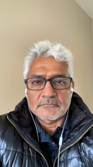 A middle-aged Indian man is making a video call and wearing earbuds