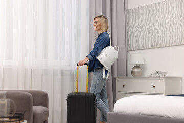 Smiling guest with suitcase and backpack exploring stylish hotel room