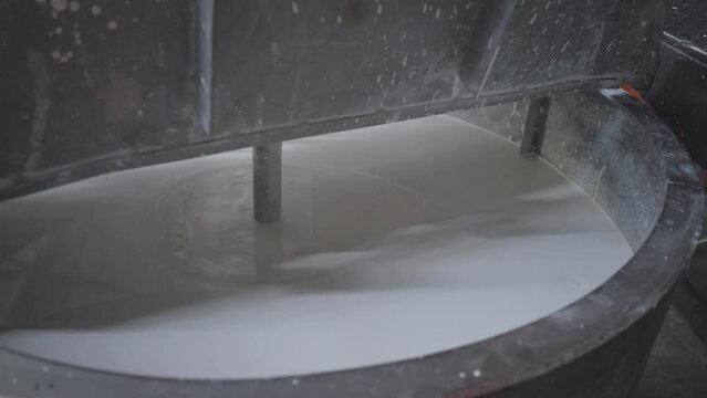 Mixing liquid clay in container barrel to produce ceramic tiles at plant. Tile chemical hardener making machine. Slip or clay slurry. Conveyer line for ceramic tile at heavy plant