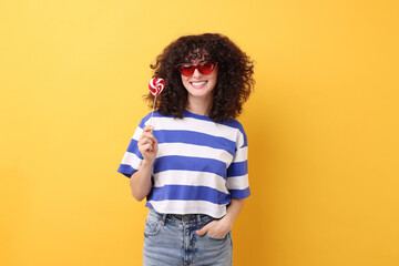 Beautiful woman in sunglasses with lollipop on yellow background