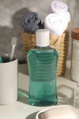 Bottle of mouthwash, toothbrush and soap on light table in bathroom