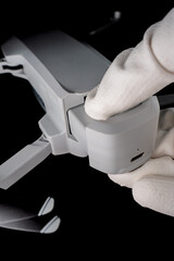 A person wearing gloves inserts a battery into a compact drone, preparing it for a flight indoors.
