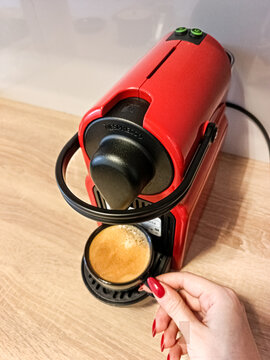 Woman hand holding a black espresso cup filled with coffee from a red  nespresso coffee machine on a kitchen counter with copy space