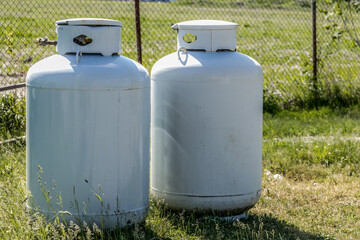 Two disconnected large vertical propane or LPG tanks resting in the grass at a construction site