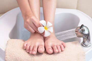 Close up, beautiful woman's hands hold flowers on her feet which are on a foot massage tub, prepare...