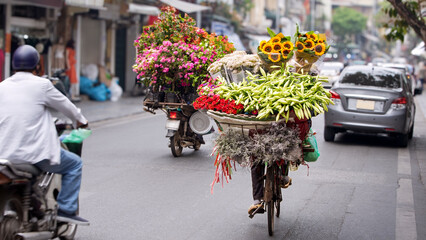 A Vietnamese street vendor woman uses her bicycle to flower stall along a road.