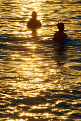 Two figures of people in the sea on the background of sunset