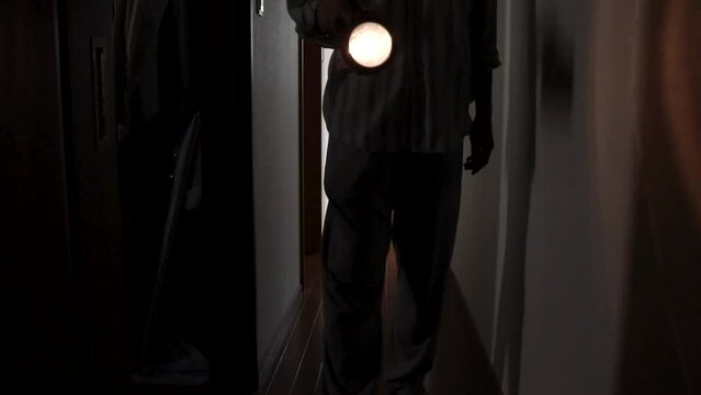 懐中電灯を手に持って暗い廊下を歩く人物