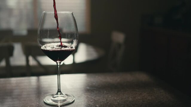 Pour red wind into glass on kitchen counter 