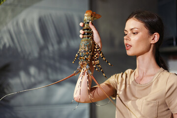 Woman holding lobster in front of window, playful and curious expression, seafood theme in natural...