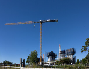 A huge tower crane and concrete pourer machinery set up for the construction of an office building with several towers, all against a blue sky providing copy space in this Australian city.