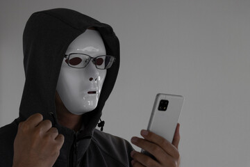 白い仮面と眼鏡をつけスマートフォンを持つ男性。握りこぶし