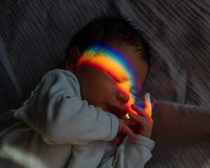 Close-up portrait of a newborn boy with a prism beam on his face. Rainbow.