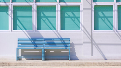 Two wooden benches in front of glass windows and blue sun blinds with sunlight and shadow of transparent polycarbonate awning on modern white concrete residential building wall surface