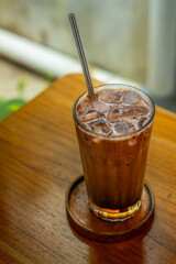 iced hazelnut and chocolate milk drink served on transparent glass, over small wooden plate, on wooden table surface