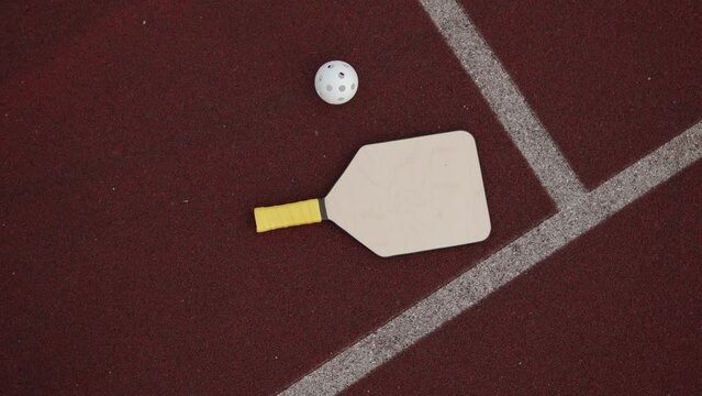 Top view of wooden pickleball racket with ball lies on rubber surface of sports field with markings. Sports equipment for playing pickleball on stadium.
