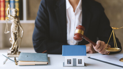 A lawyer holding a gavel next to a small house model, scales of justice, and legal books. Concept...