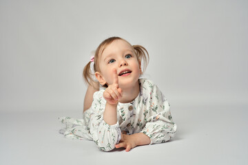 Portrait of little girl with blue eyes and blond hair wearing white dress. Cute child laying on a...