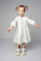 Little girl wearing high heel shoes and white dress standing on a white background