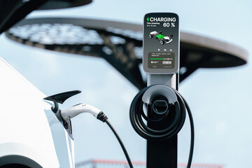 Electric car recharging battery at outdoor EV charging station for road trip or car traveling,...