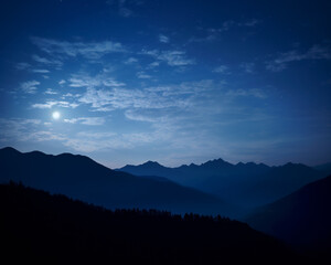 Obraz premium Serene night mountain landscape under a starry sky with moonlight casting shadows over the ridges and valleys, creating a tranquil atmosphere.